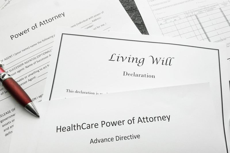 Living will declaration and power of attorney papers sitting on a desk with an ink pen on top.